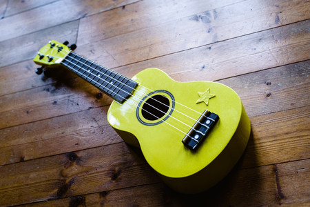 Small yellow ukulele on wooden floor ready to be played