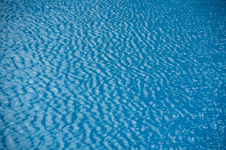 Water with small waves and raindrops on a pool with blue texture background