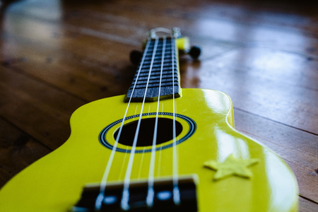 Small yellow ukulele on wooden floor ready to be played