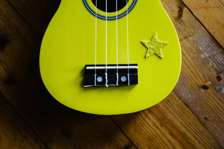 Small yellow ukulele on wooden floor ready to be played
