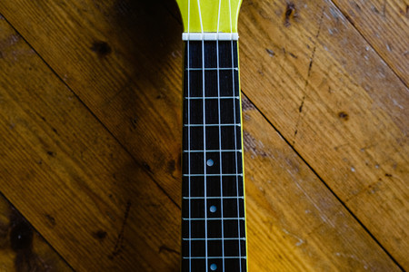 Small yellow ukulele on wooden floor ready to be played