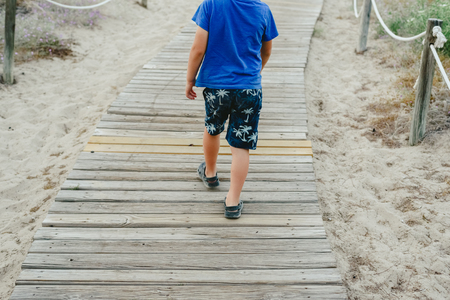 Children walking on wooden path towards the beach in summerの写真素材