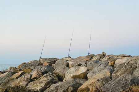 Fishing rods fixed to the rocks near the sea coast without fishermenの写真素材
