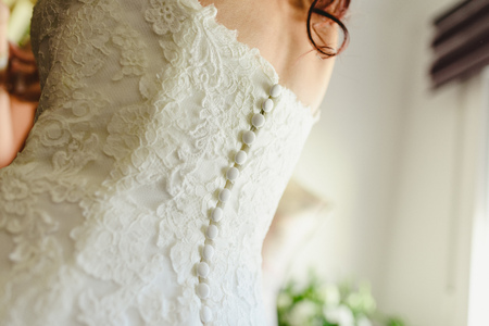 Bride getting ready, they help her by buttoning the buttons on the back of her dress.の写真素材