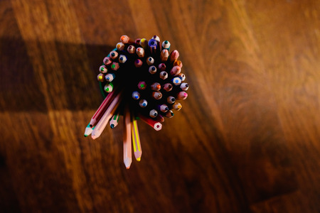 Colored pencils in a full pen, on the floor with warm wood background and free space for text