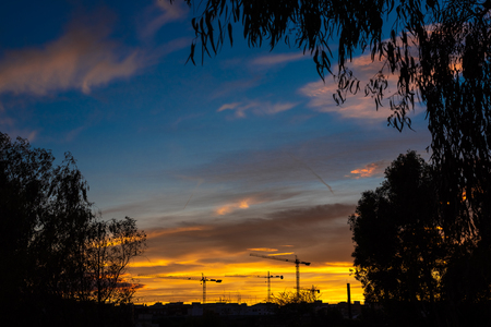 Skyline cityscape at sunset with silhouettes of building construction cranes, real estate business concept.の写真素材
