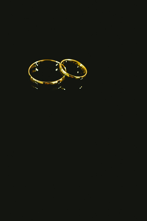 Golden wedding and love rings isolated on black backgroundの写真素材