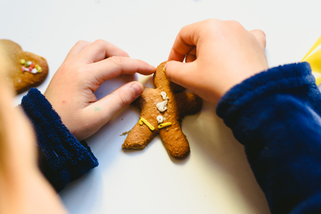 Child hands preparing homemade gingerbread cookies with colorful decorations.の写真素材
