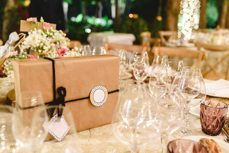 Gift box wrapped in paper and with bow and empty label to include free text, on the elegant table of the reception of a wedding, without anyone.の写真素材