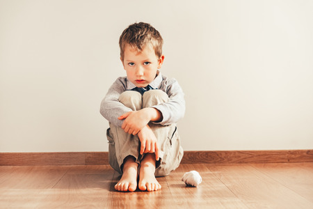 Child sitting on the floor barefoot with sad face for not being able to put on his clothes.の写真素材