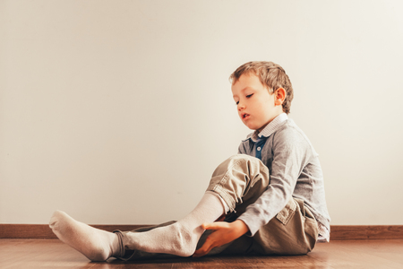 Child with lots of independence sitting on the floor putting on his socks with an expression of effortの写真素材