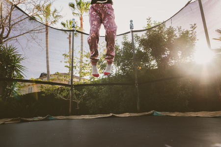 Little girl enjoying her vacation jumping on the trampoline doing acrobatic exercise outdoors.の写真素材