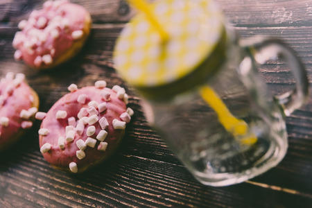 Jug of juice with colorful straw and pink glazed donuts on wooden board.の写真素材