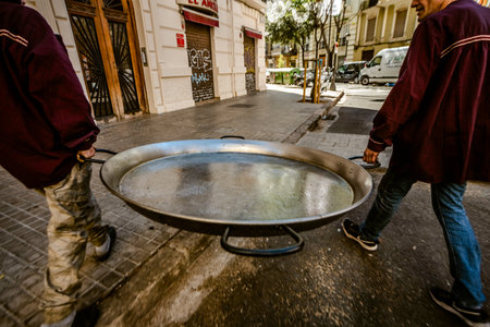 Valencia, Spain - March 19, 2019: Two chefs transport a huge paella pan to prepare the traditional Valencian rice.のeditorial素材