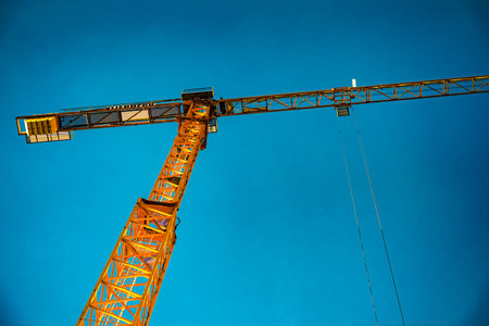 Two large tower cranes for building construction, view from below against blue sky.のeditorial素材