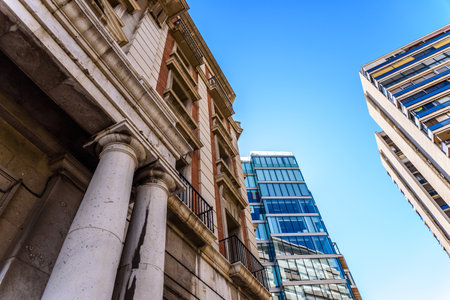 Old building in the foreground in front of modern business office buildings with large glass windows, blue sky background .のeditorial素材