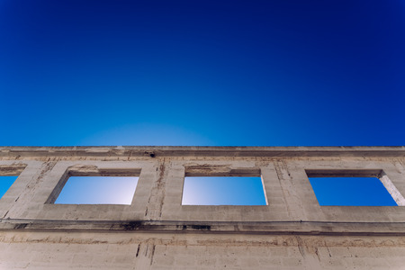 Window of abandoned building without finishing its construction, intense sun and deep blue sky background.の写真素材