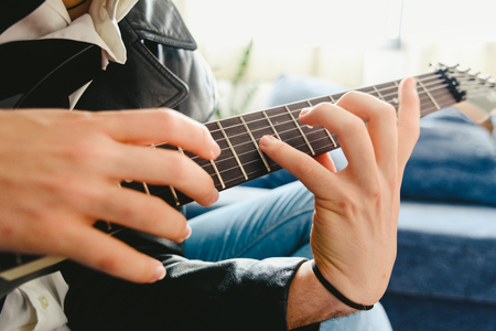 Young man practicing with his electric guitar on the sofa of his house learning.の写真素材