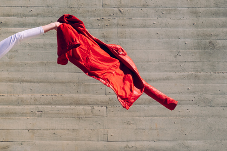 Arm of young woman waving her red jacket with a gray background copy space.の写真素材