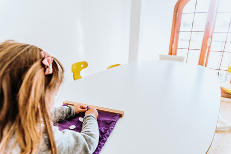 Girl buttoning a montessori frame to develop the dexterity of her fingers.の写真素材