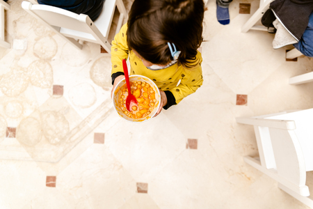 Girl walking with a bowl of stew in the dining room of her nursery school, top view, with copy space.の写真素材