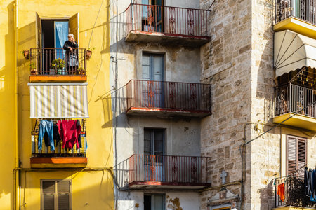 Bari, Italy - March 10, 2019: Older woman leaning on the balcony of her colorful house.のeditorial素材