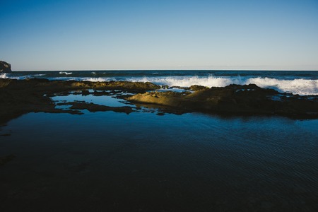 Small waves of a calm sea reaching the shore with rocks at dusk, deep blue sky background.の写真素材