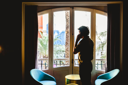 Entrepreneur man attending a phone call in his office in front of a large window.のeditorial素材