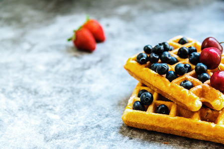 Close-up of a waffle with blueberries and strawberries with delicious aspect, isolated on abstract background with copy space for text.
