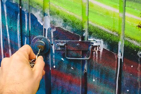 Man's hand using a key to open the lock of a door of an abandoned garage.の写真素材