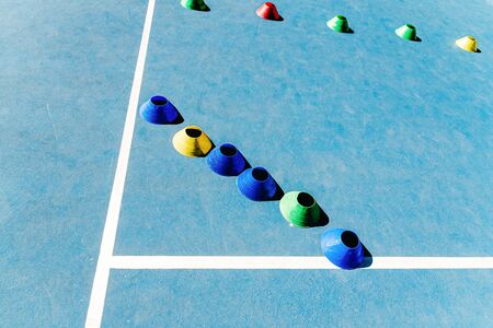 Colorful plastic cones on a blue cement tennis court with white lines background.の写真素材