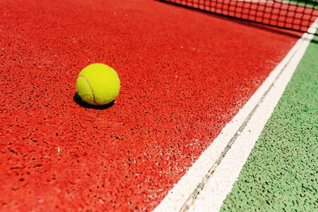 Yellow tennis ball on the red cement court to the sun, summer sports.の写真素材