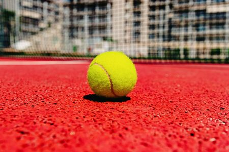 Yellow tennis ball on the red cement court to the sun, summer sports.の写真素材