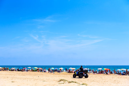Valencia, Spain - June 23, 2019: Police in quad patrolling a beach full of tourists and holiday makers to avoid thefts and thefts typical of the summer time.のeditorial素材