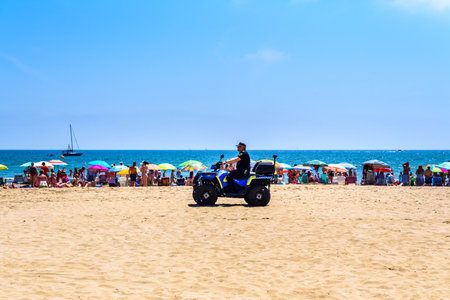 Valencia, Spain - June 23, 2019: Police in quad patrolling a beach full of tourists and holiday makers to avoid thefts and thefts typical of the summer time.のeditorial素材