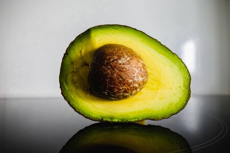 Avocado, cross section, with its reflection in a black surface of a kitchen.の写真素材