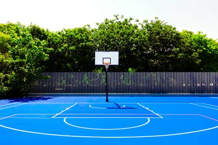 Basketball court in an outdoor park, with intense midday sun, nobody, and blue painted floor.の写真素材