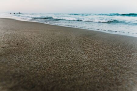 Small waves reach the shore of a serene beach and wet the fine sand, background of tranquility and vacations, at sunset.の写真素材
