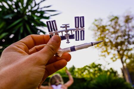 Space station figurine and rocket held with one hand against the sky, concept of space conquest.