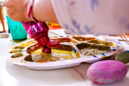 Little girl with brush dipping in a brightly colored paint palette.の写真素材