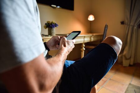 Man working remotely with his mobile phone in a hotel room.の写真素材
