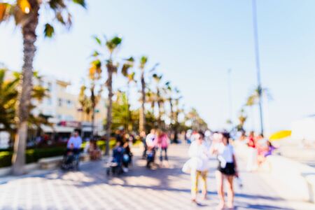 Defocused scene to use as background of a promenade with palm trees and tourists vacationing.