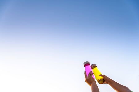 Happy kids toasting with toy bottles of vibrant colors with blue sky background.の写真素材