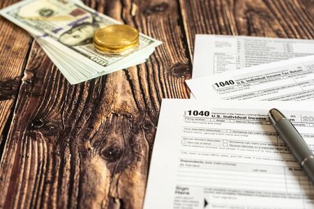Dollar bills on a table in which the 1040 American tax payment form is filled out.
