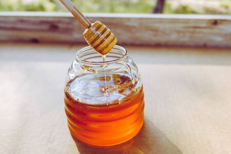 Wooden spoon honey Dipper, dripping honey inside the jar, unfocused background with copy space.