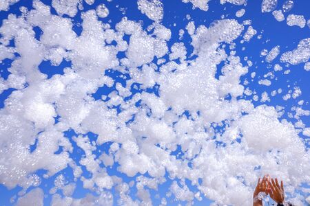 Group of happy people raise their hands during a foam party in summer to play with soap bubbles.の写真素材