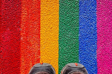 A man steps on his boots with the gay flag, painted on the ground, a concept of contempt for rights.