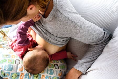 Close-up portrait of adorable and sweet newborn baby breastfeeding, holding moms finger with his...