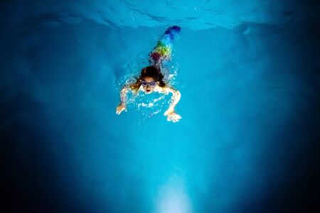 Mermaid diving towards the light of a blue pool at night, with a dreamlike background of fantasy and imagination.の写真素材