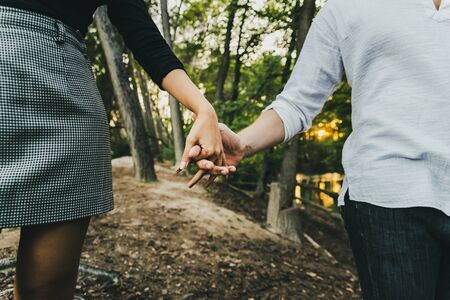 Close-up of the intertwined hands of a couple in love walking through a forest.の写真素材